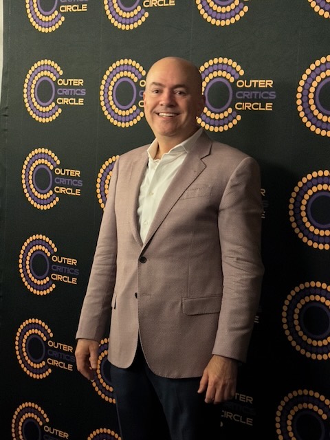 Brian Guy at the Outer Critics Circle Awards in front of the awards backdrop